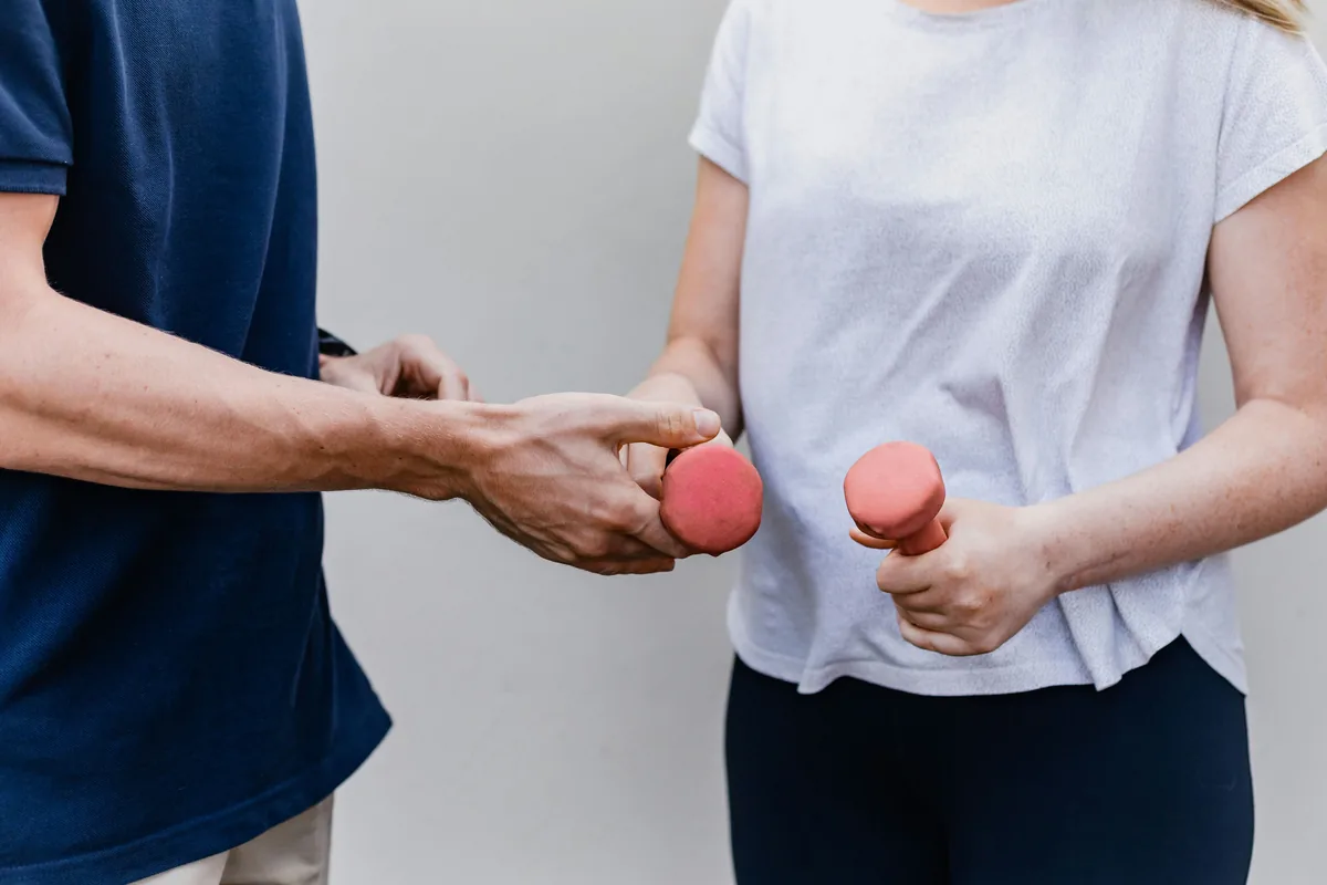 Physiotherapeut reicht einer Patientin Hanteln fürs Training